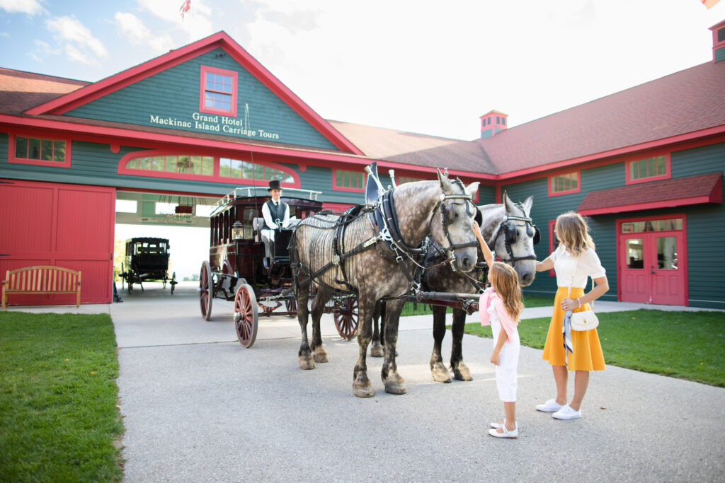 A mother and daughter petting carriage horses - The Grand Hotel Hospitality Marketing