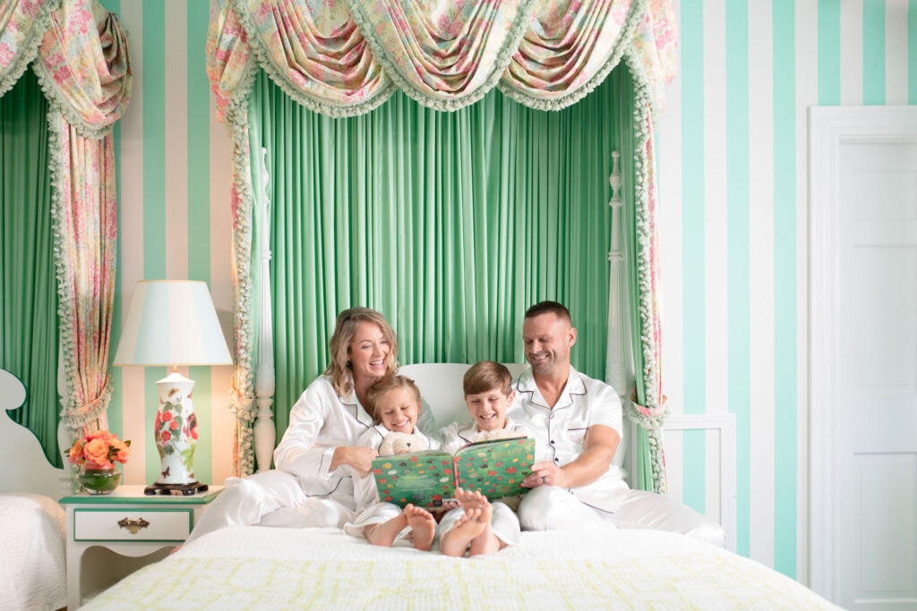 A family of four reading a book in bed with green tones and matching sleepwear - The Grand Hotel Hospitality Marketing