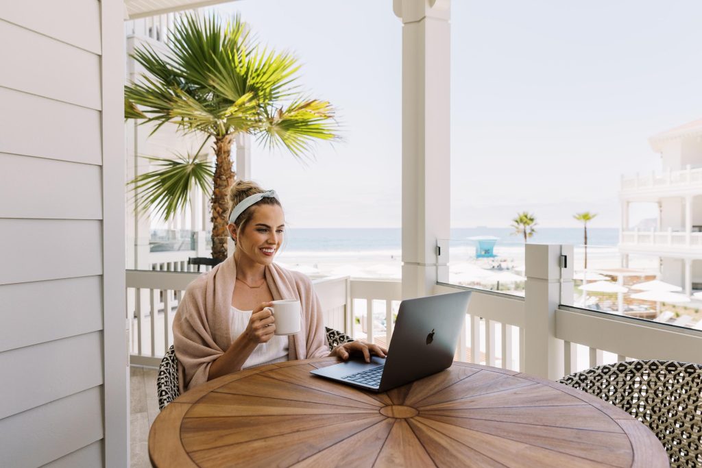A young woman enjoying a cup of coffee on her lap top next to a hotel beach - Hotel Photography - Shore House at the Del