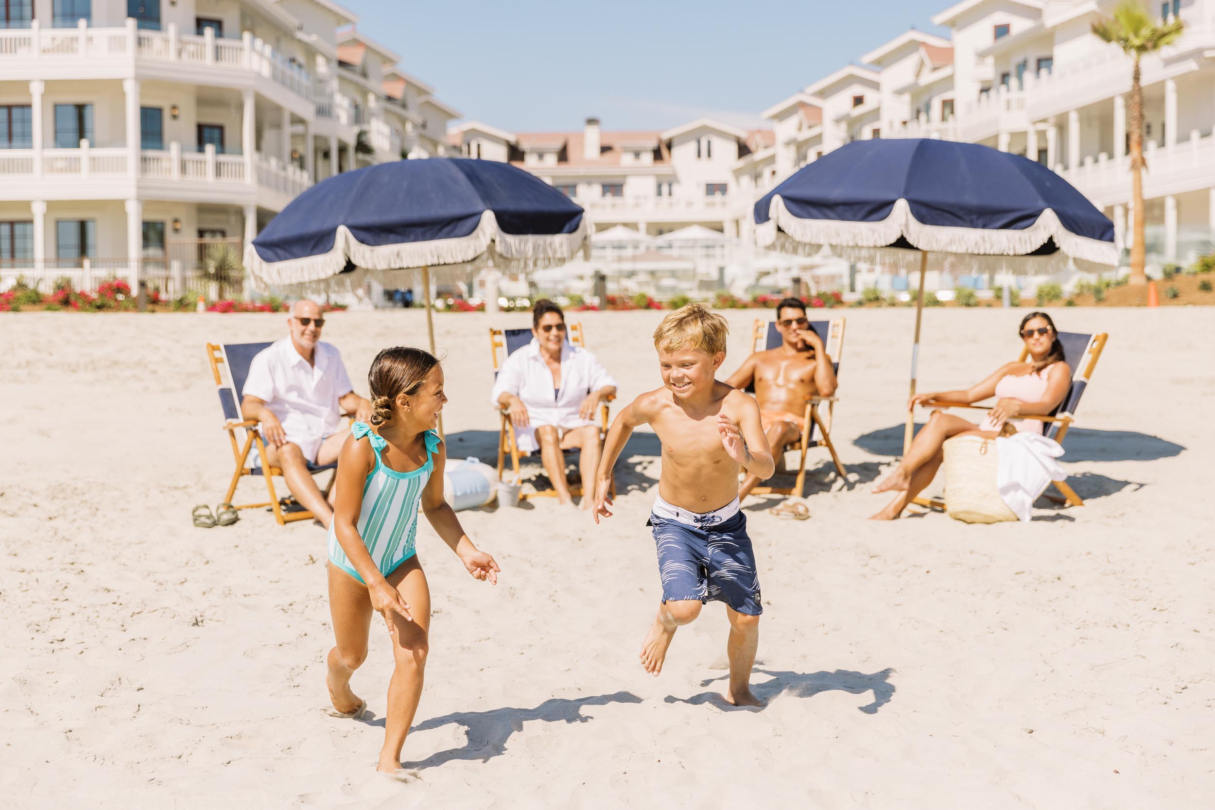 A young family watching two children run on the beach - Hotel Photography - Shore House at the Del